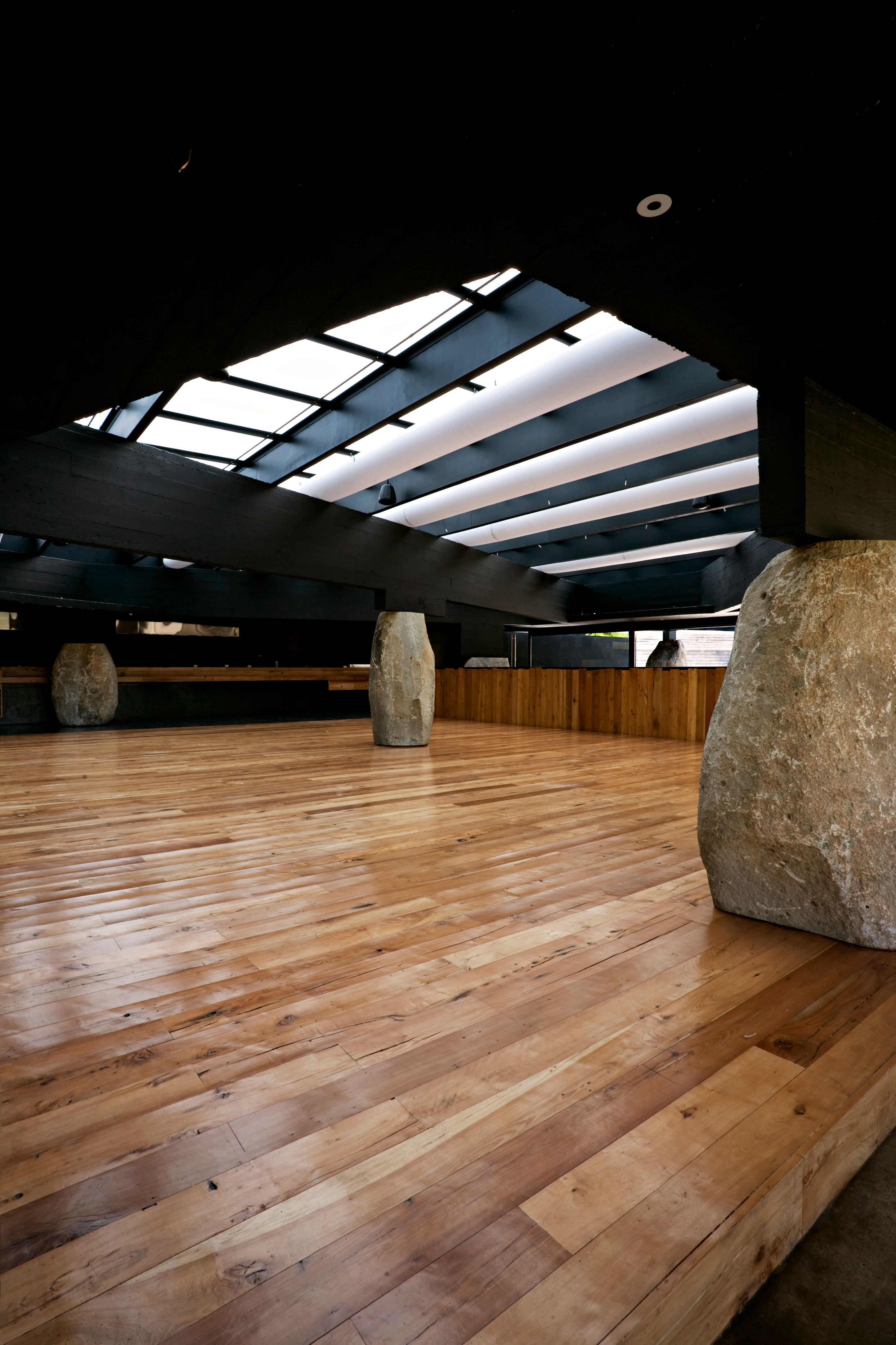 El salón bajo los lucernarios: piso de madera nativa y rocas como pilares.